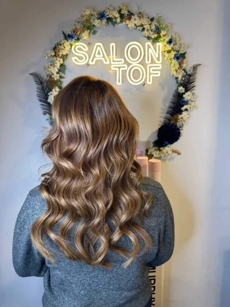 Klant met golvend bruin haar voor het verlichte naambord van Salon TOF